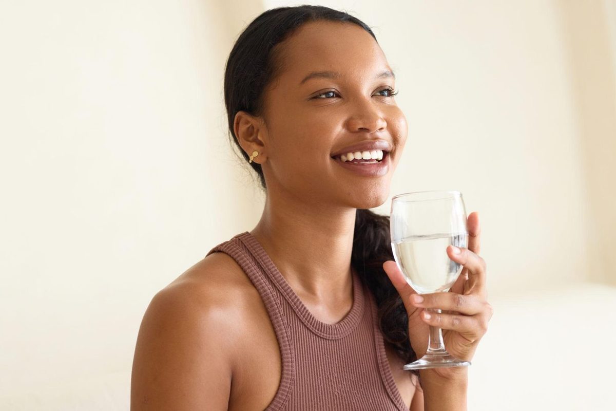Jeune femme souriante buvant un verre d'eau NAFI